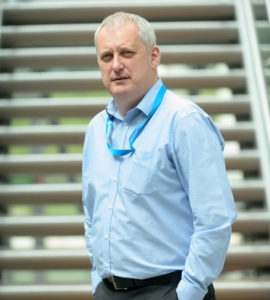 John Milne is standing in front of a stairs at the NIBRT office and smiling into the camera.